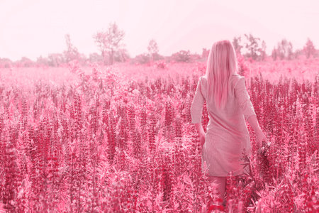 Beautiful blonde young woman in a field with blooming lupines