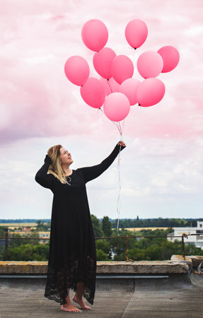 Young cheerful woman with balloons on the roofの写真素材