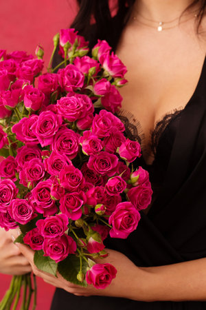 A young woman in a black dressing gown with a deep neckline holds a bouquet of pink roses, on a pink background, close-up, on a pink background.の写真素材