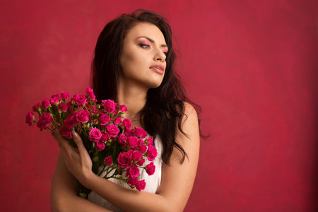 A beautiful young woman is holding a bouquet of pink roses on a pink backgroundの写真素材