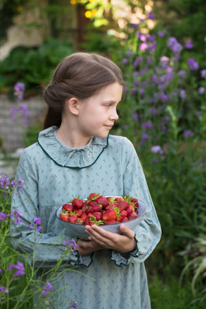 Cute little girl in a vintage dress with a bowl of ripe strawberries in the gardenの写真素材