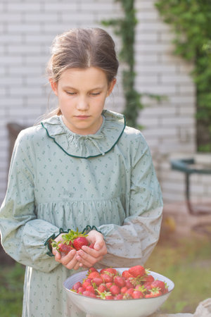 Cute little girl in a vintage dress with a bowl of ripe strawberries in the gardenの写真素材