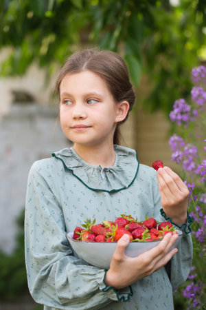 Cute little girl in a vintage dress with a bowl of ripe strawberries in the gardenの写真素材