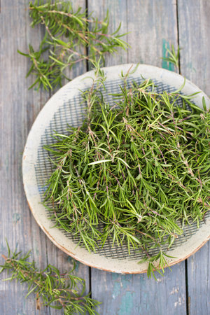 Sprigs of aromatic rosemary in a gray bowl on a wooden backgroundの写真素材