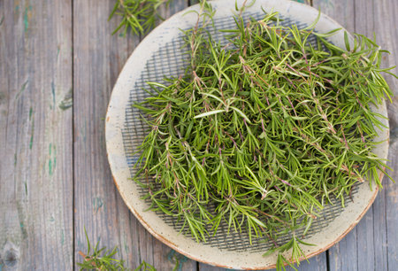 Sprigs of aromatic rosemary in a gray bowl on a wooden backgroundの写真素材