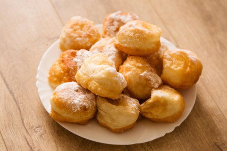 Ruddy fragrant donuts sprinkled with powdered sugar in a plate on a wooden backgroundの写真素材