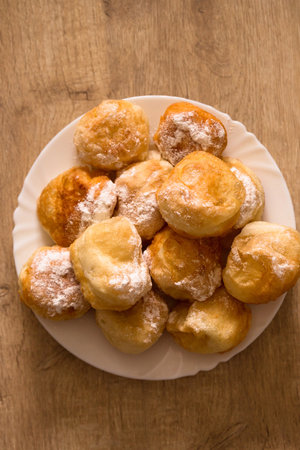 Ruddy fragrant donuts sprinkled with powdered sugar in a plate on a wooden backgroundの写真素材