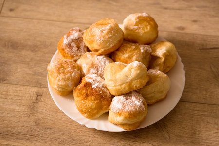 Ruddy fragrant donuts sprinkled with powdered sugar in a plate on a wooden backgroundの写真素材