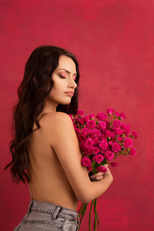 A beautiful young woman is holding a bouquet of pink roses on a pink background.の写真素材