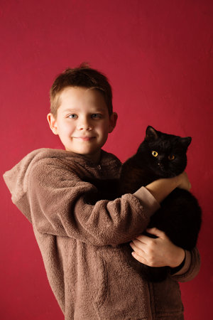 Portrait of a boy holding a domestic black cat on a pink backgroundの写真素材