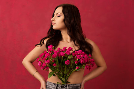 A beautiful young woman is holding a bouquet of pink roses on a pink background.の写真素材