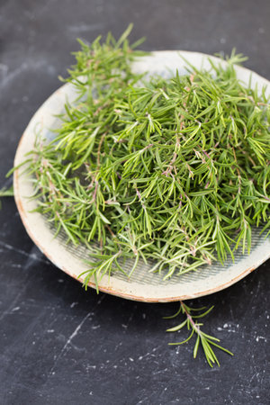 Sprigs of aromatic rosemary in a gray bowl on a wooden backgroundの写真素材