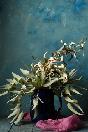 A beautiful bouquet of eucalyptus branches in a blue carafe against the background of blue wall in a rustic styleの写真素材