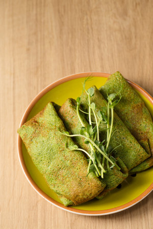 Green pancakes from spinach and young pea shoots in a plate on a wooden tableの写真素材