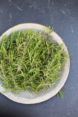 Sprigs of aromatic rosemary in a gray bowl on a wooden backgroundの写真素材