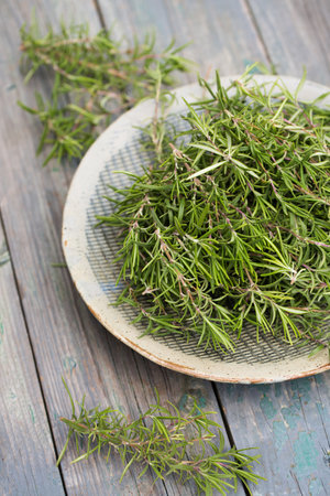Sprigs of aromatic rosemary in a gray bowl on a wooden backgroundの写真素材