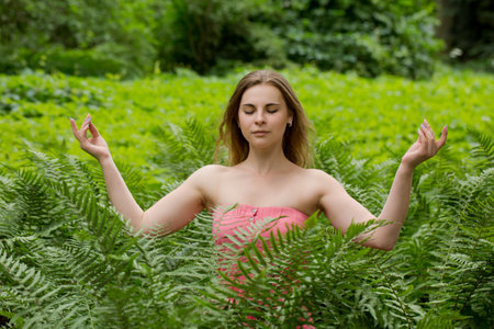 Young beautiful woman meditating in nature among fern leaves in the green forestの写真素材