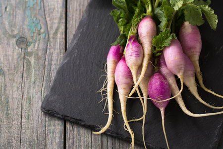 Fresh spring radish with purple-white skin and herbs on a wooden boardの写真素材