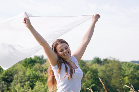 A happy young woman with a white cloth in her hands catches the wind in natureの写真素材