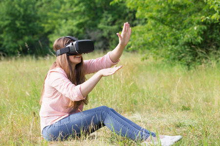 Young beautiful woman wearing virtual reality glasses having fun outdoorsの写真素材