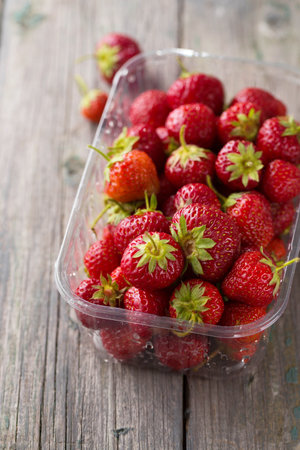 Juicy ripe red strawberry in a plastic container on a wooden backgroundの写真素材