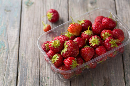 Juicy ripe red strawberry in a plastic container on a wooden backgroundの写真素材