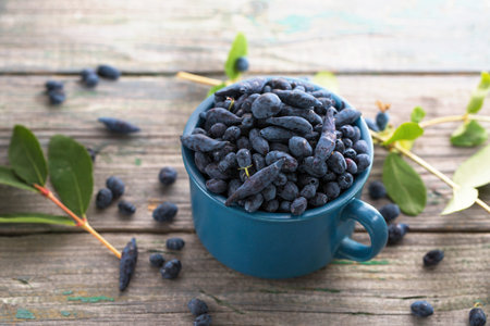 Juicy ripe honeysuckle in a blue cup on a wooden backgroundの写真素材