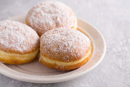 Ruddy delicious donuts berliners with filling sprinkled with powdered sugar on a white plate on a gray backgroundの写真素材