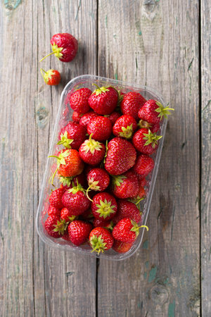 Juicy ripe red strawberry in a plastic container on a wooden backgroundの写真素材