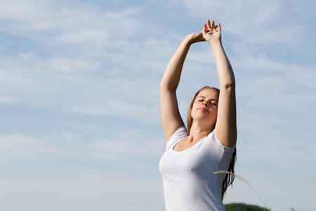 Happy, free woman standing with arms raised, saluting the sun outdoorsの写真素材