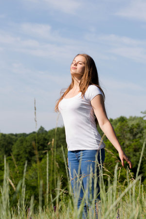 Happy, free woman standing with arms raised, saluting the sun outdoorsの写真素材
