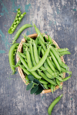 Ripe fresh green peas in a wicker basket on a rustic backgroundの写真素材