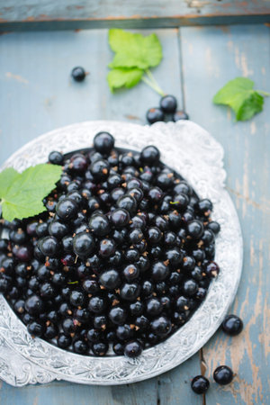 Ripe black currants in a vintage metal tray on a wooden background.