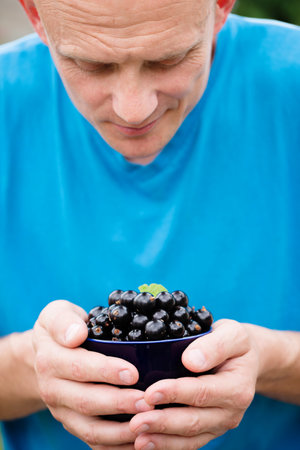 A man holds a large cup with ripe black currants in his hands, close-upの写真素材