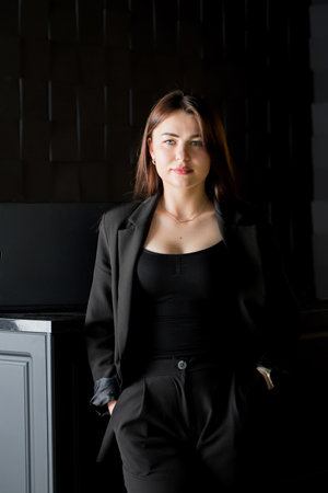 Beautiful young confident woman in black office suit in dark interiorの写真素材