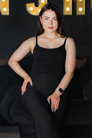 Beautiful feminine young woman in a black T-shirt and pants in a dark interiorの写真素材