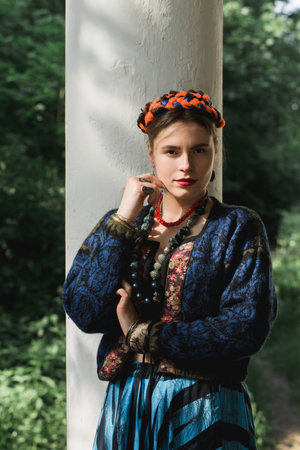 Beautiful young woman with braids on her head and a necklace near the white column in the garden