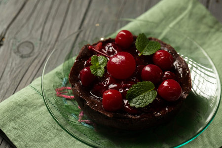 Delicious chocolate dessert with lingonberry jam, cherries and mint on a transparent plateの写真素材