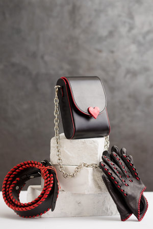 Still life of a set of a handbag, belt and gloves made of black leather with red inserts on a brick pedestalの写真素材