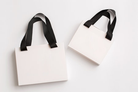 Two white paper gift bags with black handles on a white backgroundの写真素材