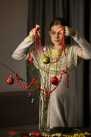 The girl decorates a bouquet of branches with an ecological garland of rose hips, made by herselfの写真素材