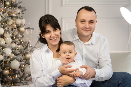 Happy young married couple with a small child near the Christmas treeの写真素材