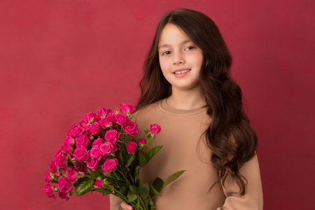 Beautiful dark-haired girl with a bouquet of small pink roses on a pink backgroundの写真素材