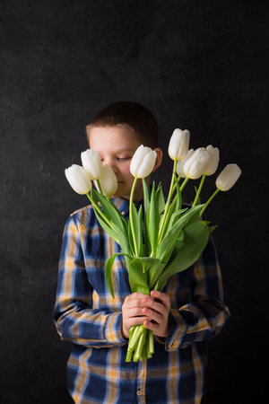 The boy is holding a bouquet of white tulips on a black backgroundの写真素材