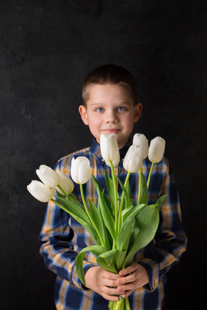 The boy is holding a bouquet of white tulips on a black backgroundの写真素材