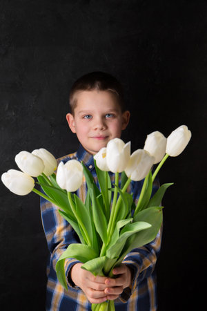 The boy is holding a bouquet of white tulips on a black backgroundの写真素材