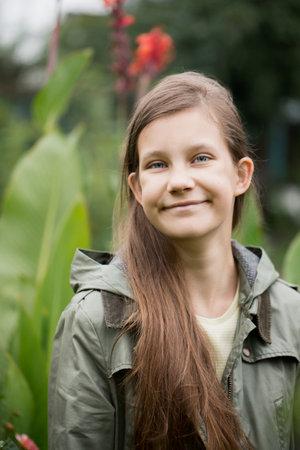 Girl teenager with long brown hair is smiling. She is standing in front of a plant with red flowersの写真素材