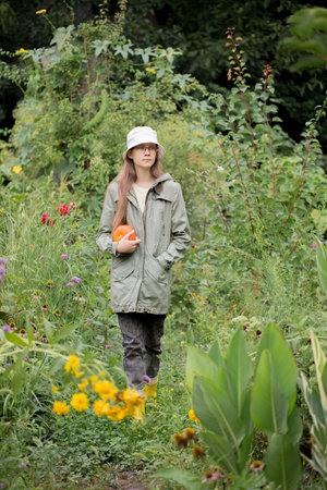 Girl wearing a green jacket and a white hat holding an orange pumpkinの写真素材