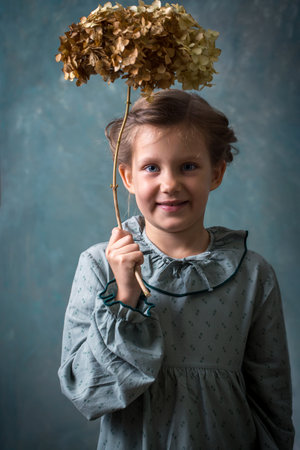 A young girl is holding a branch with a hydrangea flower. She is wearing a green dress and a collar.の写真素材