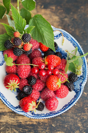 Ripe raspberries, strawberry and wild blackberries on a vintage plateの写真素材
